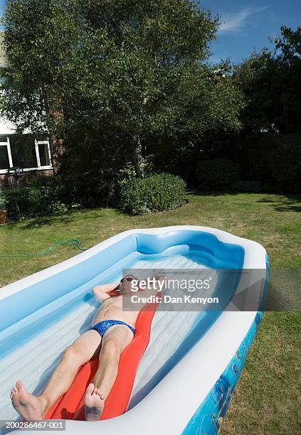 mature man sunbathing on inflatable bed in large paddling pool - pool raft imagens e fotografias de stock