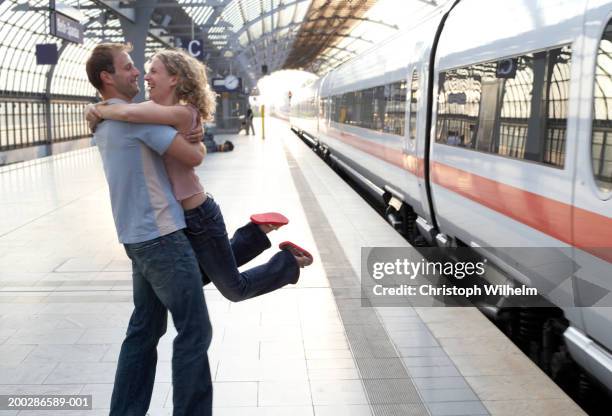 couple embracing on station platform, man lifting woman, side view - paar mittleren alters stock-fotos und bilder