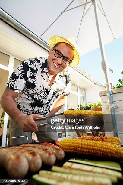 man roasting corn and sausage on grill, smiling - tang stockfoto's en -beelden