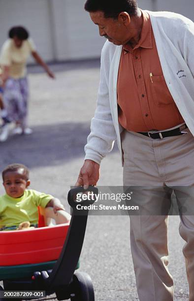 grandfather pulling grandson in cart in street - bollerwagen mann stock-fotos und bilder