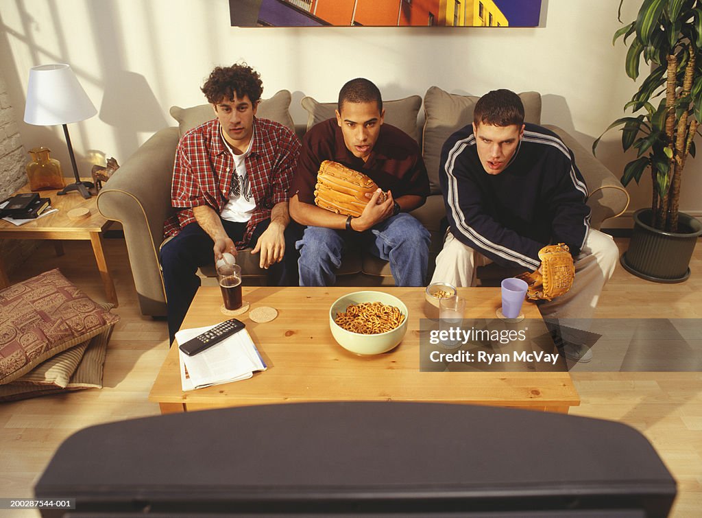 Three young men sitting watching television in flat, elevated view