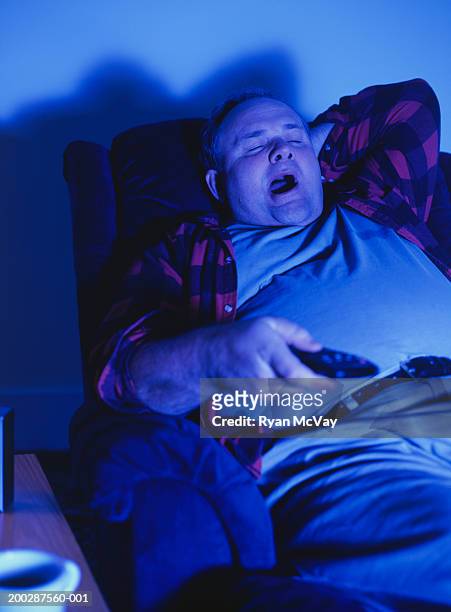 man sitting in armchair yawning, watching television in living-room - yawning foto e immagini stock