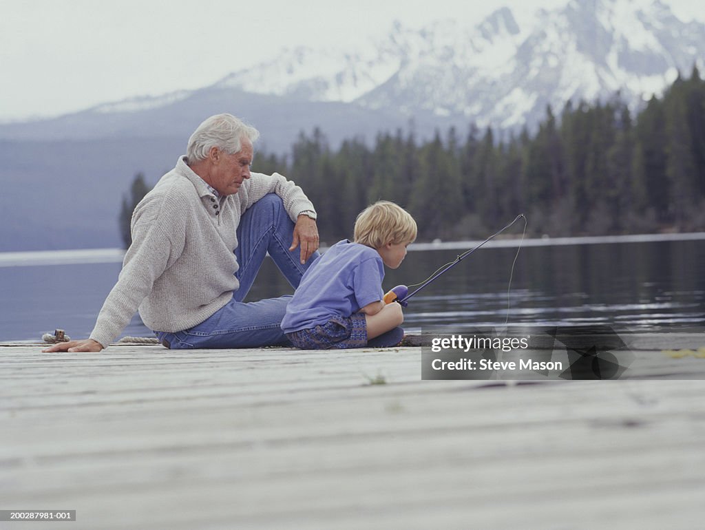 Grandfather and grandson (6-7) fishing on pier at lake