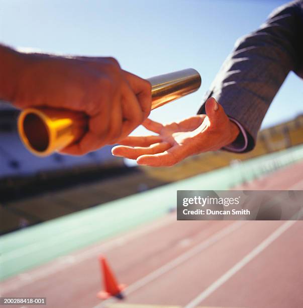 two men passing golden baton in stadium, close-up - baton stock-fotos und bilder