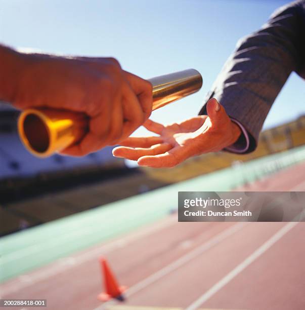 two men passing golden baton in stadium, close-up - relay baton stock pictures, royalty-free photos & images