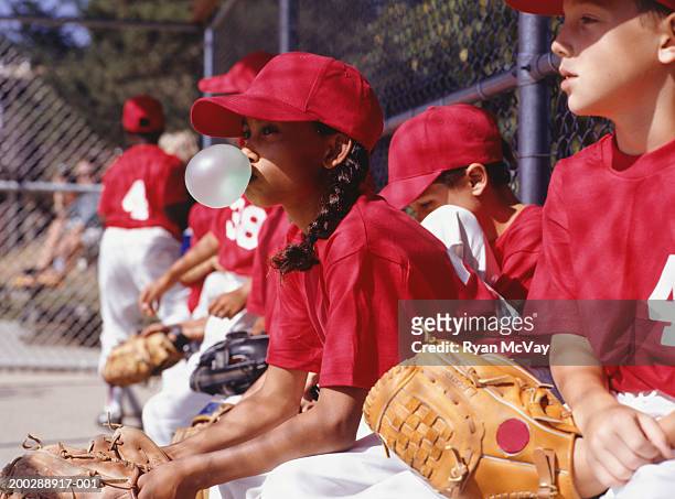 children (8-9) wearing baseball uniforms sitting in dugout, side view - baseball kid stock-fotos und bilder