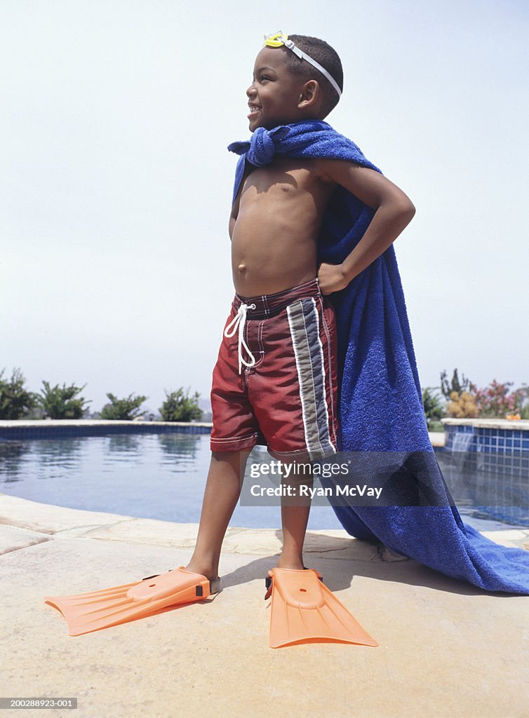 Boy (4-5) wearing towel as cape, standing by pool