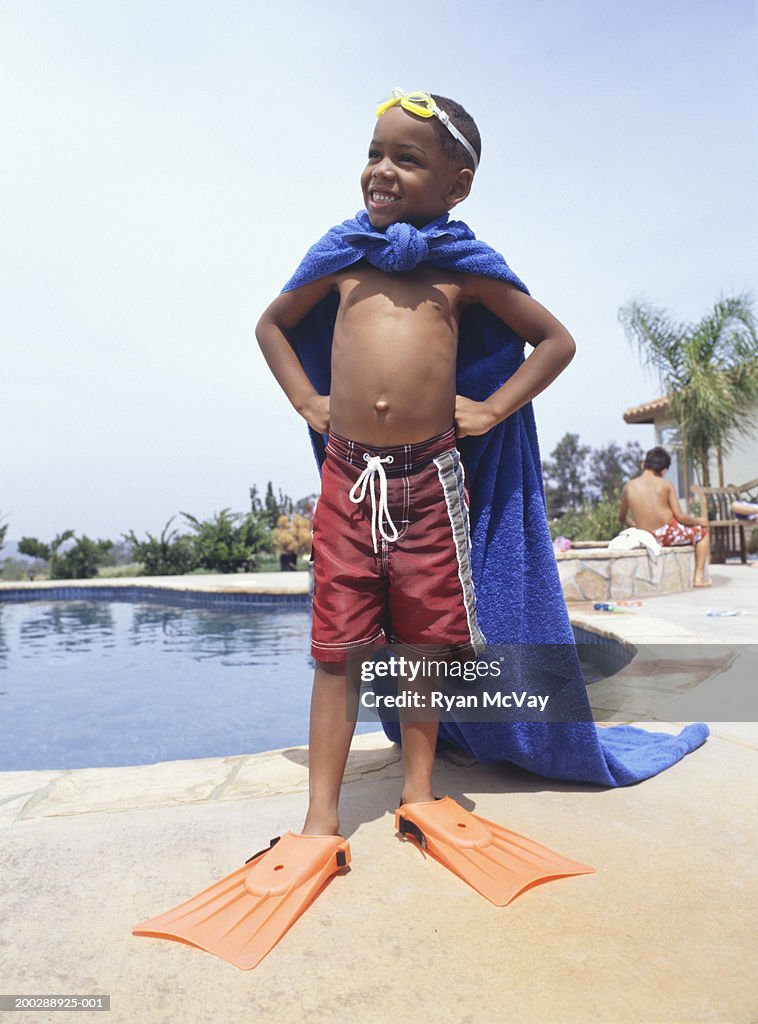 Boy (4-5) wearing towel as cape, standing by pool