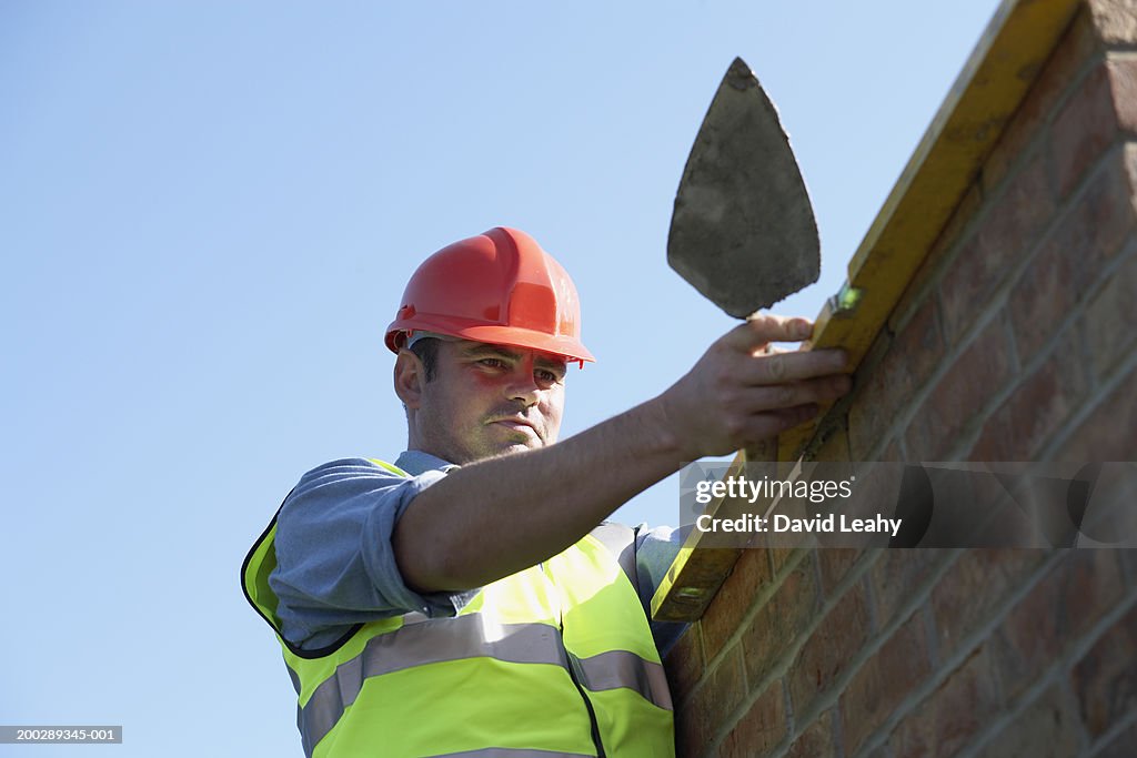 Bricklayer checking wall with spirit level, low angle view