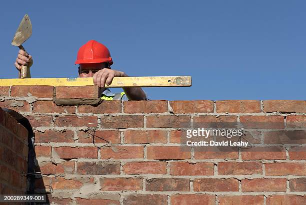 bricklayer checking wall with spirit level - brick wall building stock pictures, royalty-free photos & images
