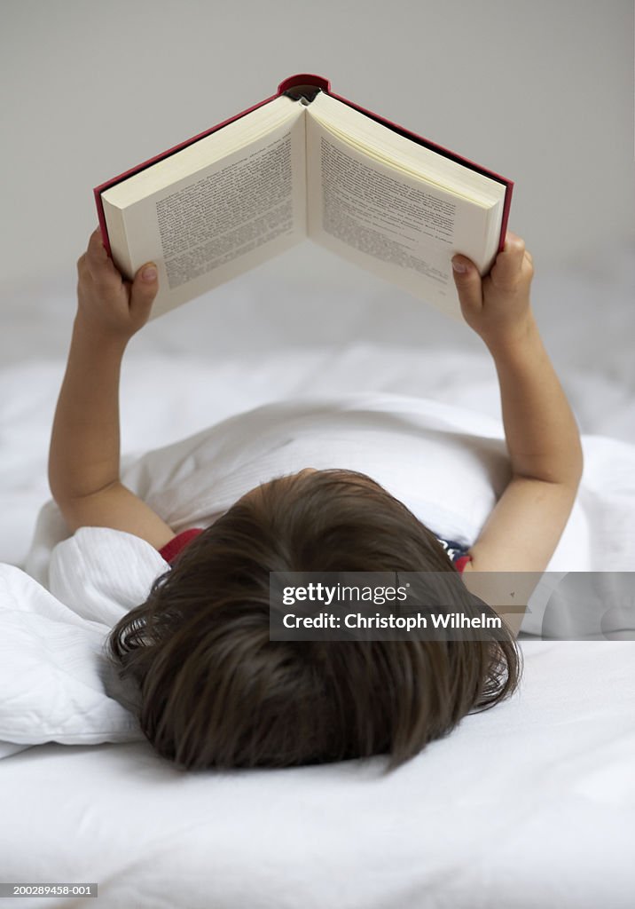 Boy (4-6) reading book in bed, rear view