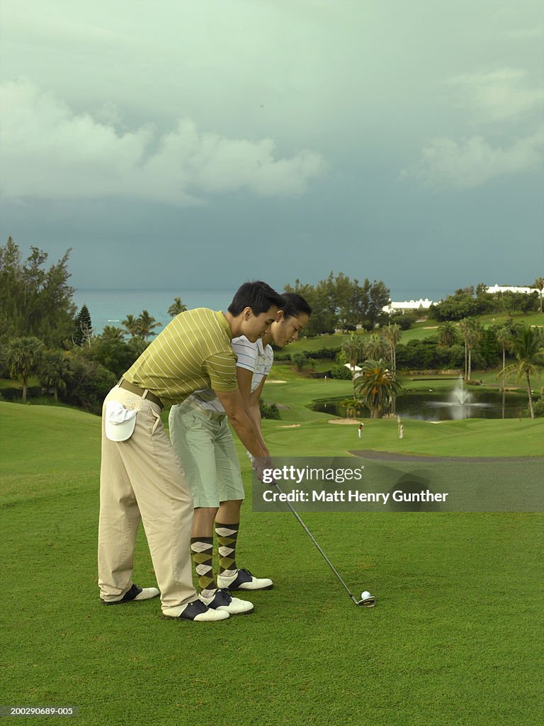 Young couple playing golf, man coaching woman, side view