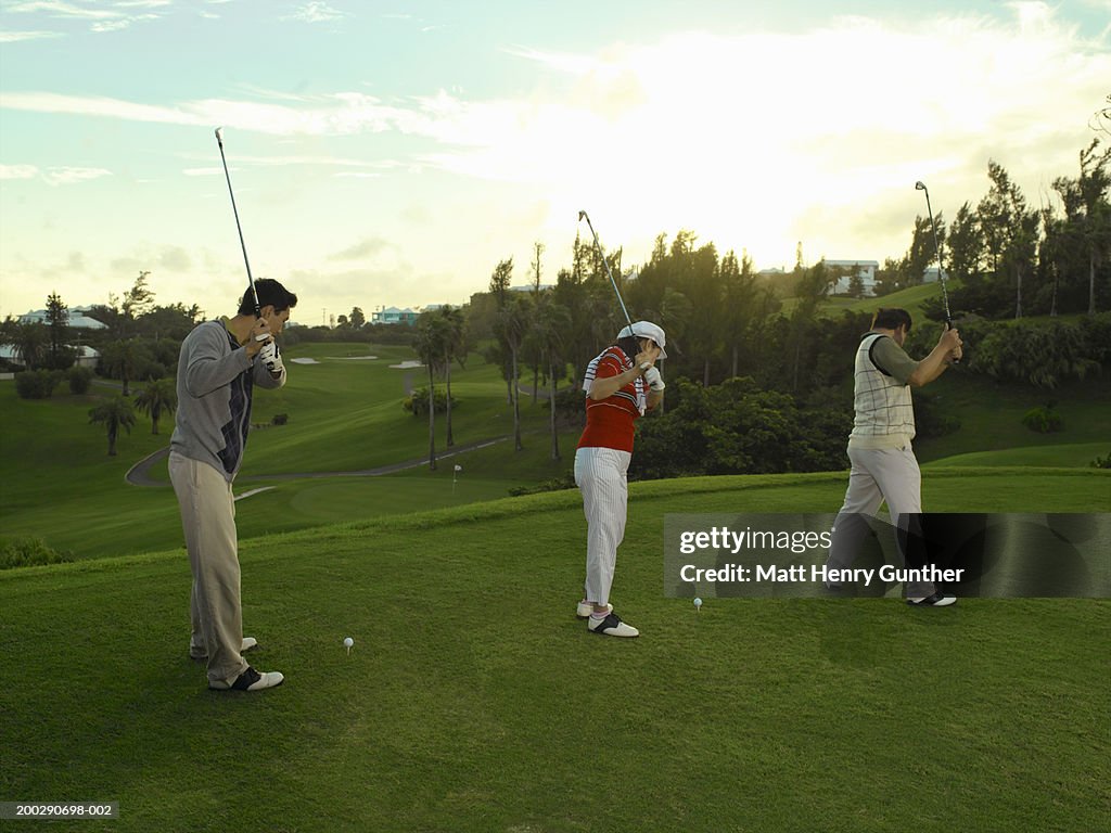 Young man and mature couple practicing driving golf ball, side view