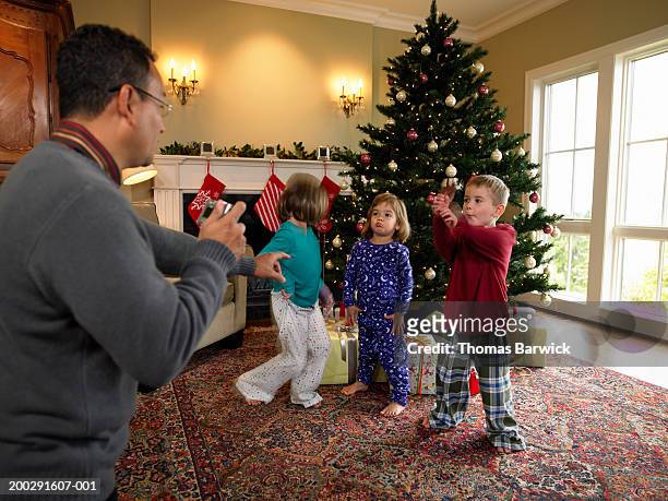 father photographing three children (3-6) beside christmas tree - kids mess carpet fotografías e imágenes de stock