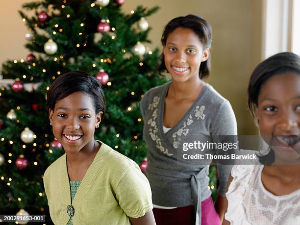 three sisters (11-15) in front of christmas tree, smiling, portrait - young sister stock pictures, royalty-free photos & images