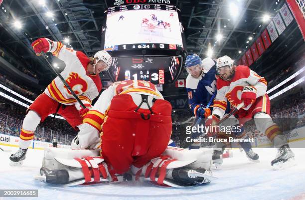 Noah Hanifin, Jacob Markstrom and Chris Tanev of the Calgary Flames defend against Kyle Palmieri of the New York Islanders at UBS Arena on February...