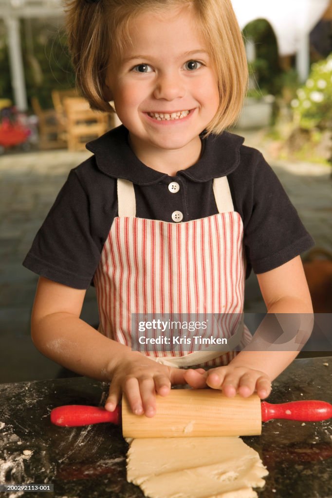 Girl (4-6) rolling dough with rolling pin, smiling, portrait