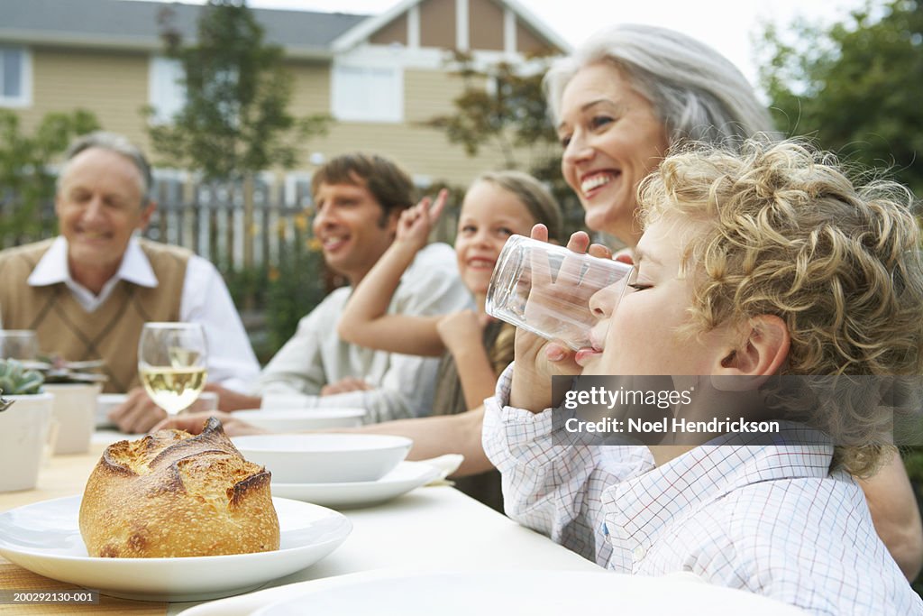 Family dining in garden, boy (5-7 years) drinking in foreground, side view