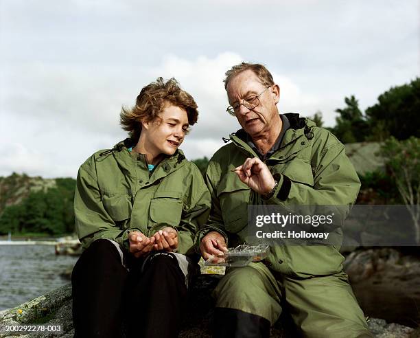 senior man showing teenage grandson (13-15) fishing hooks outdoors - two boys talking stock-fotos und bilder