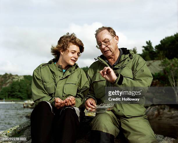 senior man showing teenage grandson (13-15) fishing hooks outdoors - wisdom stock pictures, royalty-free photos & images