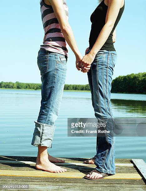 two young women holding hands on jetty, side view - rolled up trousers stock-fotos und bilder
