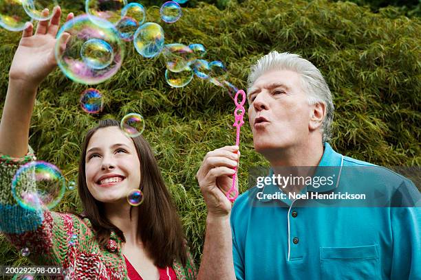 grandfather blowing soap bubbles through bubble wand, teenage girl (13-15 years) watching - 13 years old imagens e fotografias de stock
