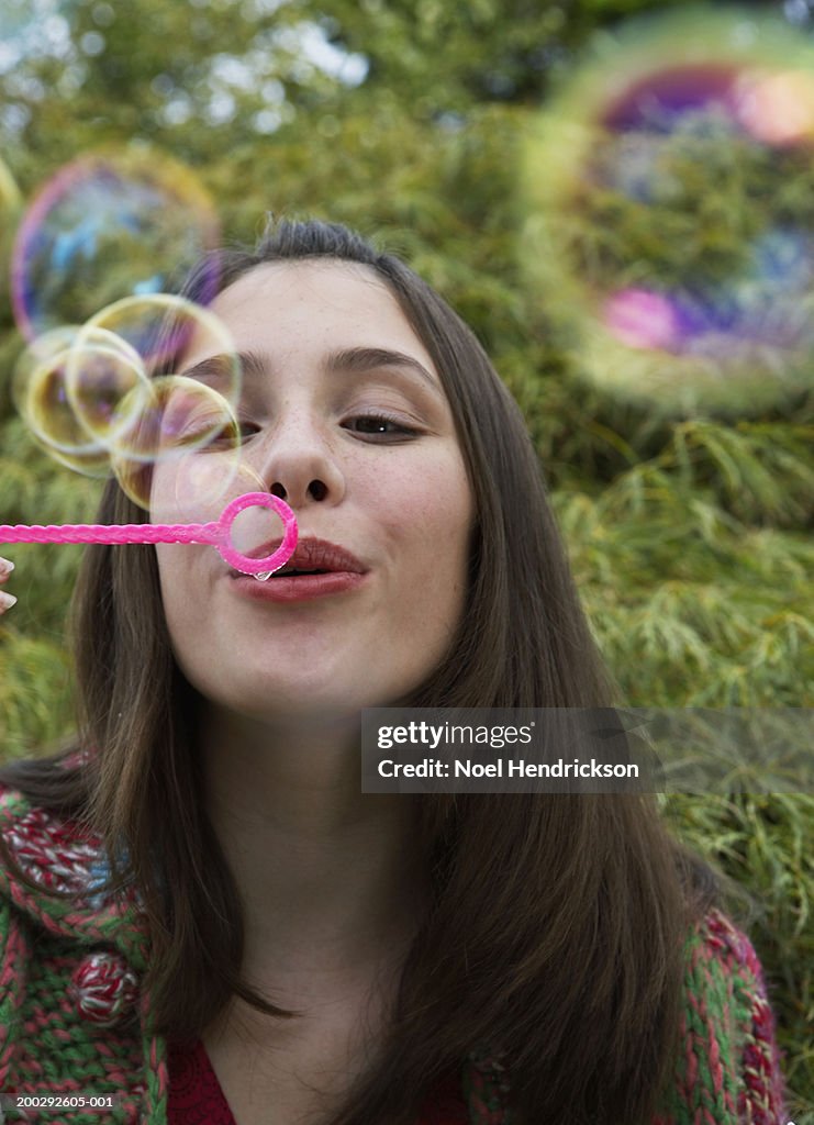 Teenage girl (13-15 years) blowing soap bubbles through bubble wand, close-up