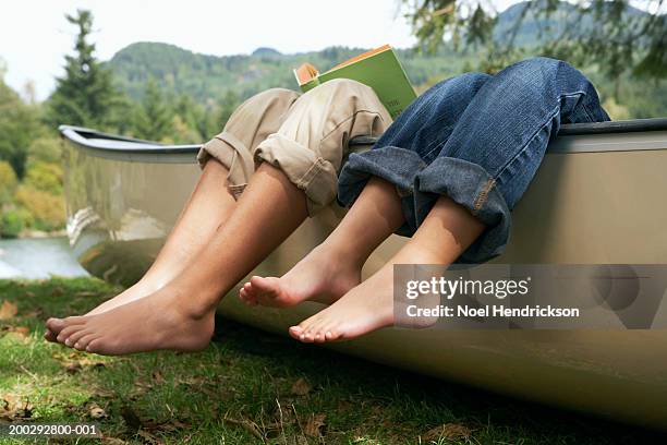 barefoot boy and girl (4-10 years) reading in canoe by lake, low section - 10 11 years boy stockfoto's en -beelden