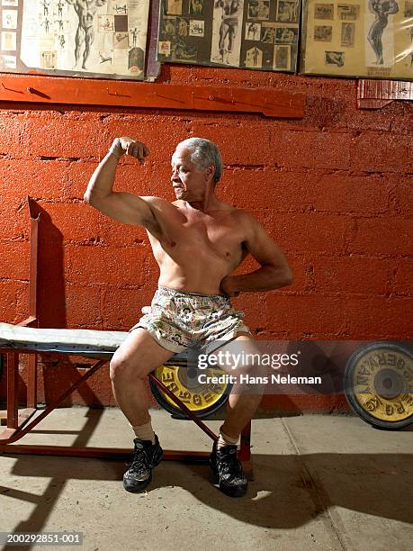 senior bodybuilder looking at flexed muscle in gym - bodybuilder flexing biceps stock pictures, royalty-free photos & images