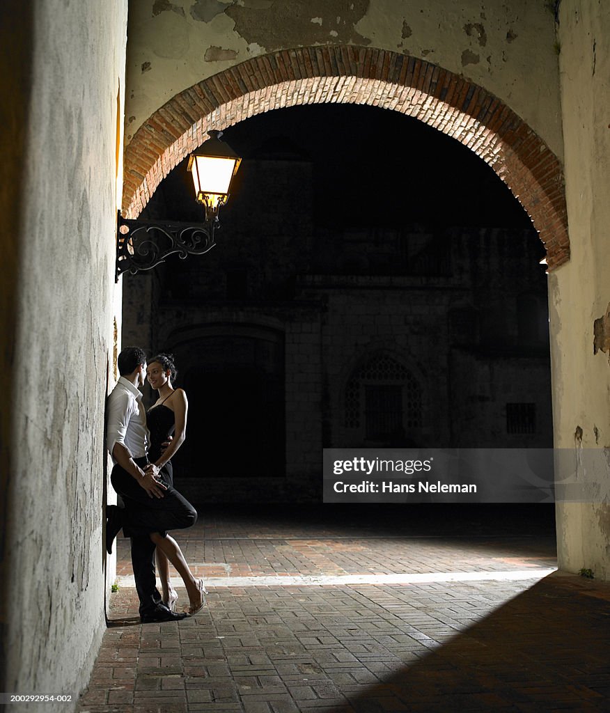 Young couple embracing under street light at night, side view