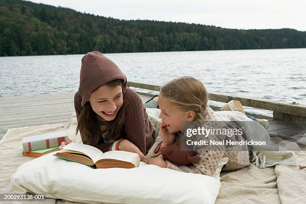 girls (6-13 years) lying on rug on jetty beside lake, reading book and laughing - 14 15 years stockfoto's en -beelden