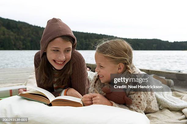 girls (6-13 years) lying on jetty beside lake, reading book together and smiling - 6 7 years - fotografias e filmes do acervo