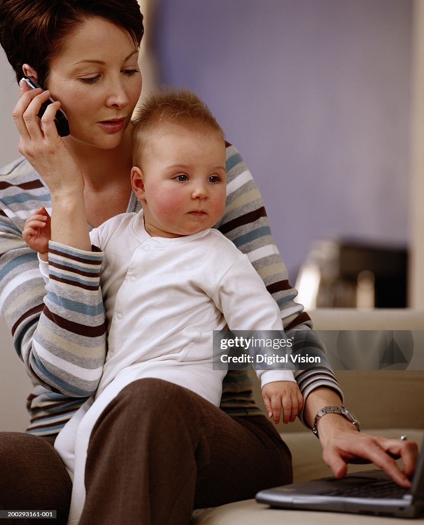 Mother holding baby girl (6-9 months), using laptop and mobile phone