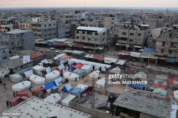 Displaced Palestinians stand outside their tents in Rafah in the southern Gaza Strip on February 14 amid the continuing battles between Israel and...