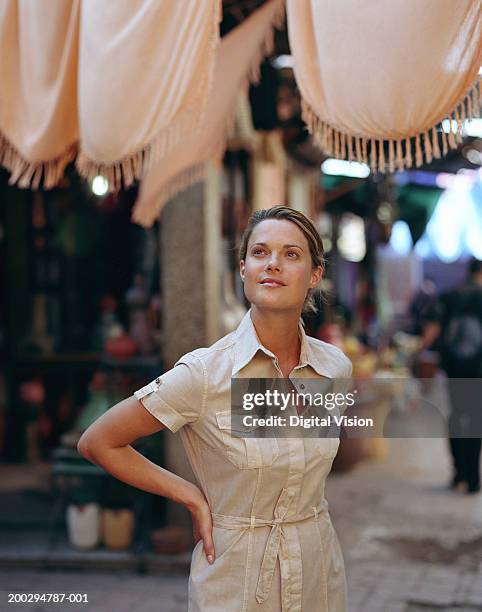 young woman standing with hands on hips, looking up - marrakech stockfoto's en -beelden