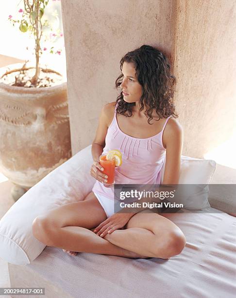 Young woman on divan indoors, holding drink, elevated view