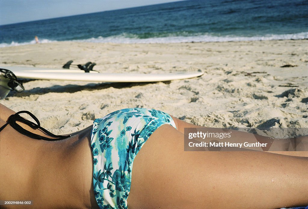 Young woman lying on beach near surfboard, mid section, side view