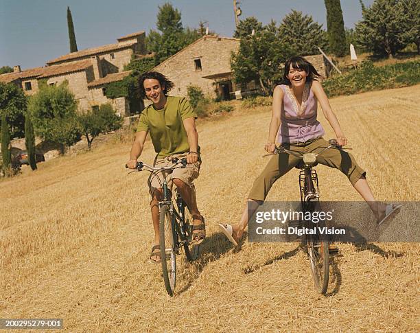 couple cycling through field, woman's legs outstretched, smiling - jambes écartées photos et images de collection