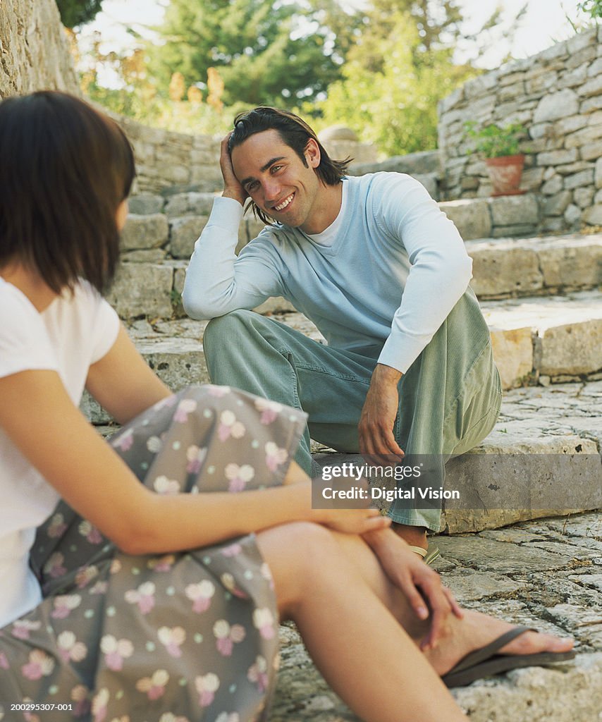 Young couple on steps outdoors, focus on man smiling at woman