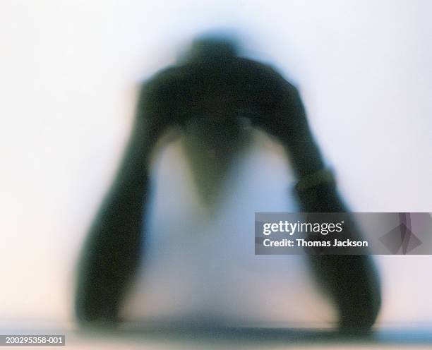 silhouette of man holding hands to temples, behind frosted glass - vouyer stock pictures, royalty-free photos & images