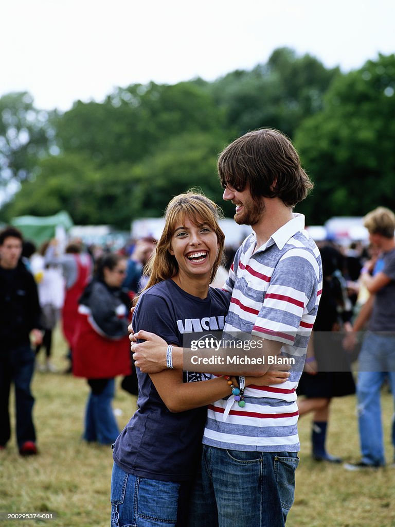 Young couple embracing at festival, woman laughing, portrait