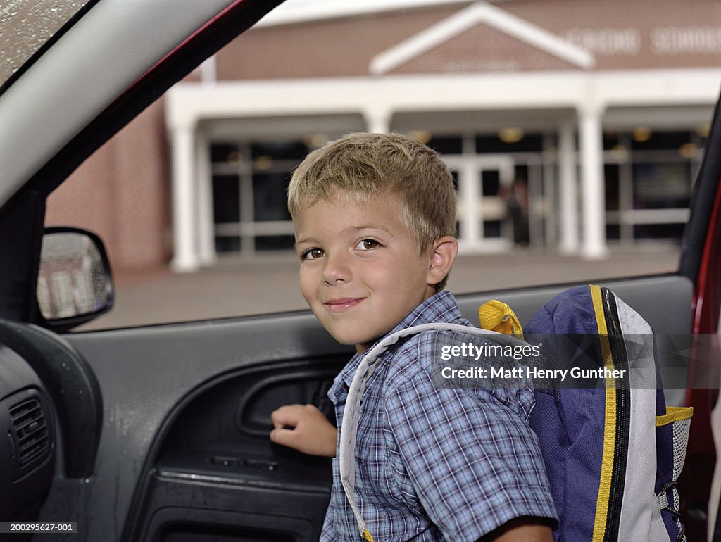 Boy (6-8) exiting car outside school, smiling, portrait
