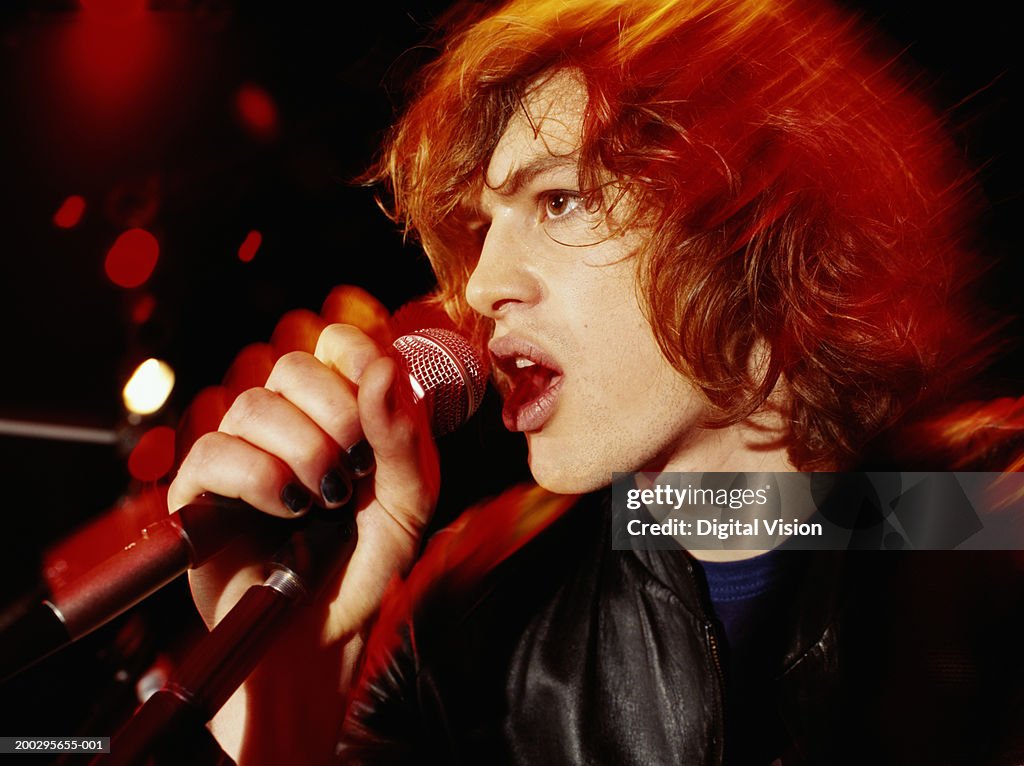 Young man singing into microphone, side view