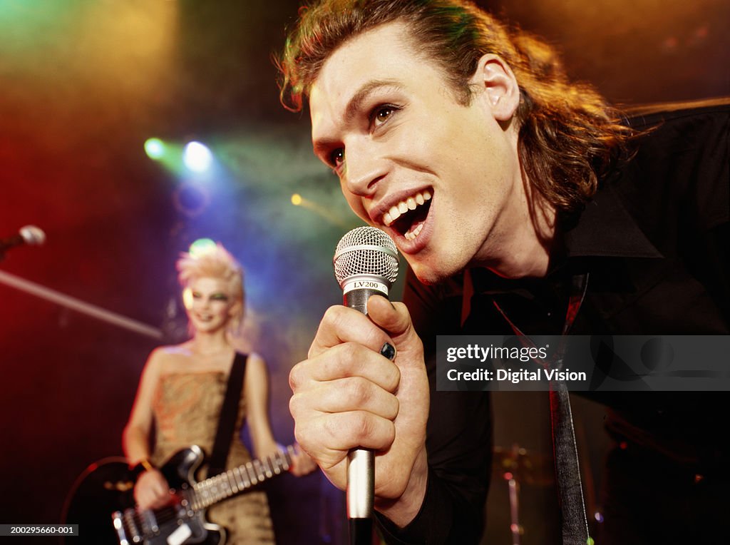 Man singing into microphone by woman playing electric guitar