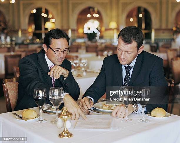 two businessmen looking at document at restaurant table, one pointing - business lunch stock-fotos und bilder