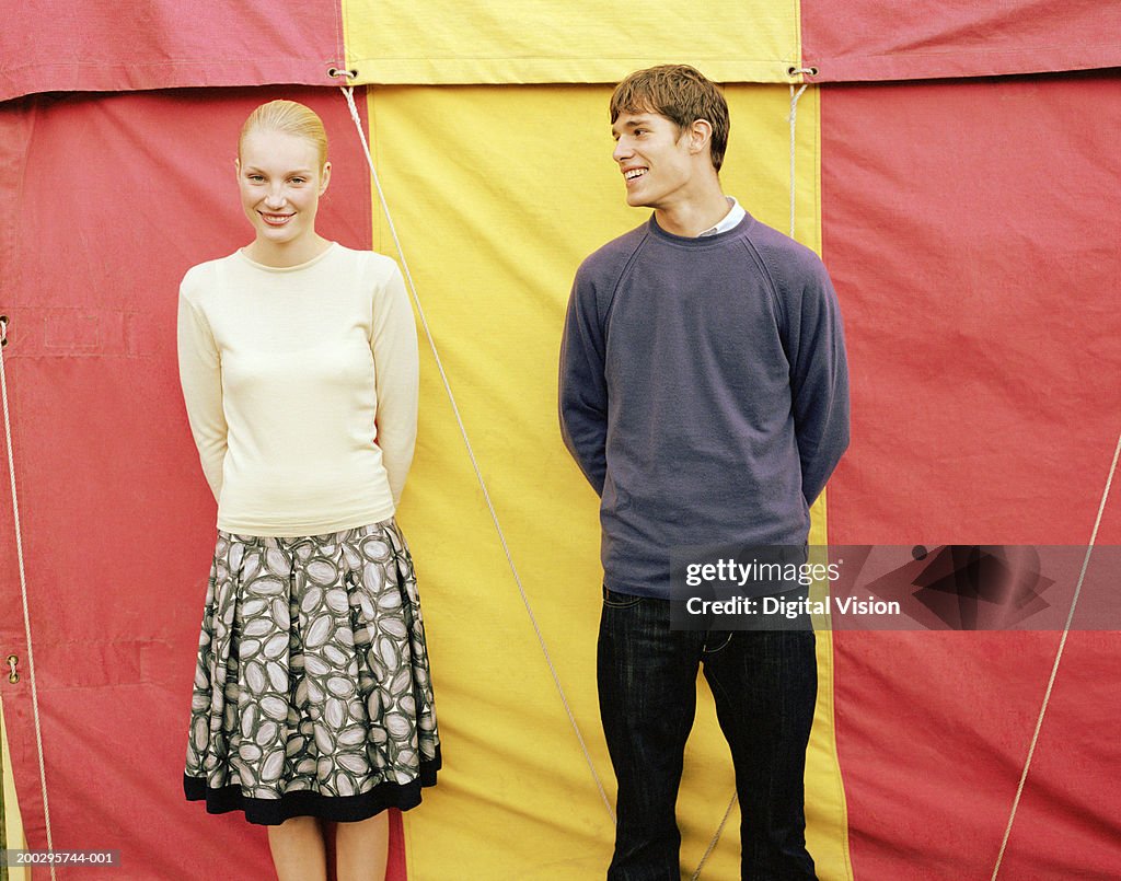 Young couple side by side in front of fairground tent, portrait of woman