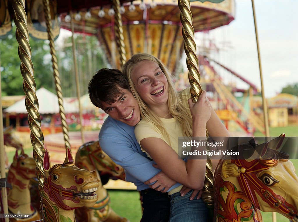 Young couple on fairground carousel, laughing, portrait