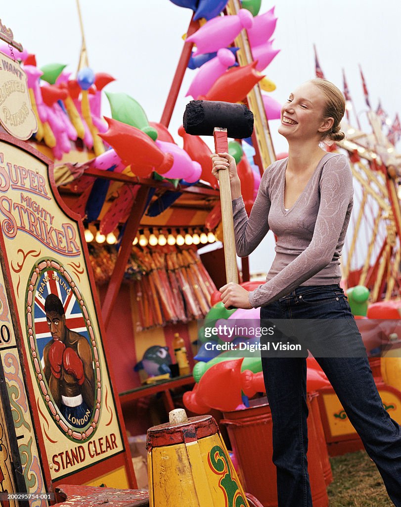 Young woman testing strength at fairground, smiling