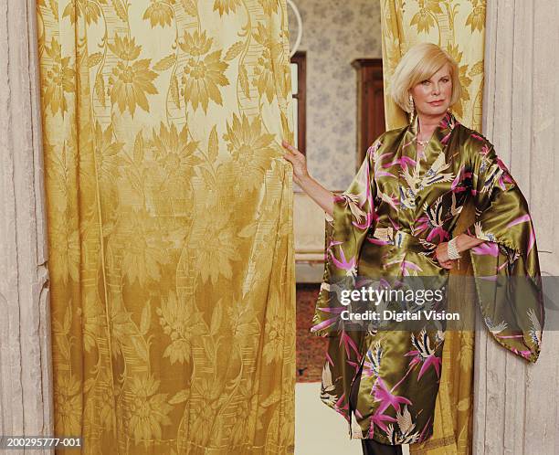 mature woman standing by curtained doorway, hand on hip, portrait - silk robe stock pictures, royalty-free photos & images