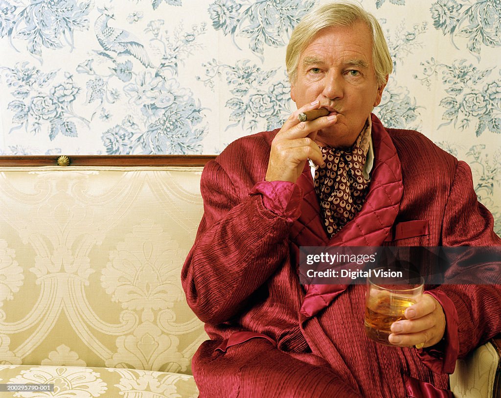 Senior man sitting on sofa, smoking cigar and holding glass, portrait